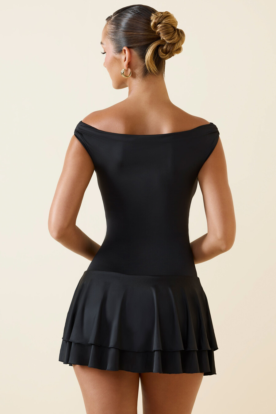 vestido curto preto com babados e ombros à mostra.